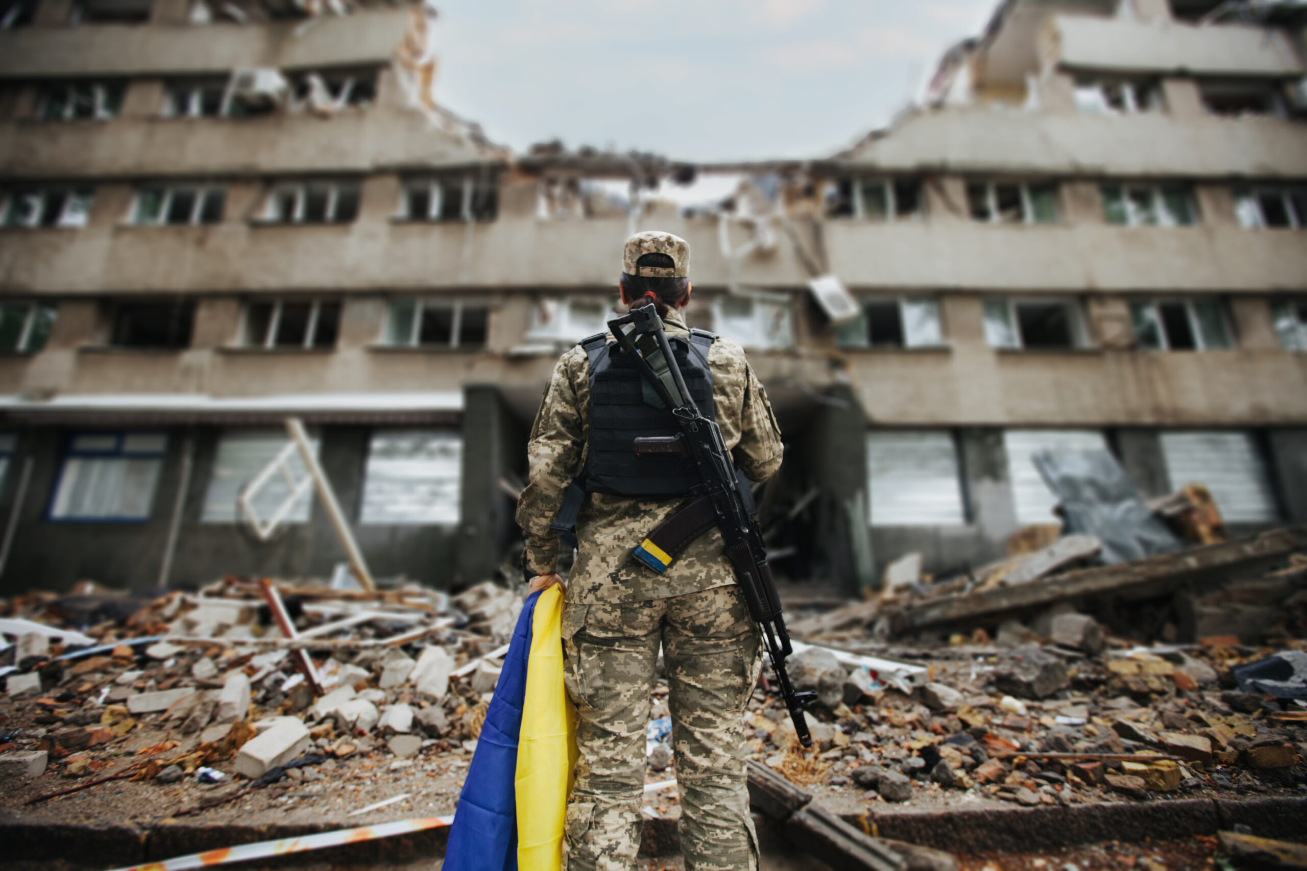 Ukrainischer soldat steht mit Flagge vor Trümmern