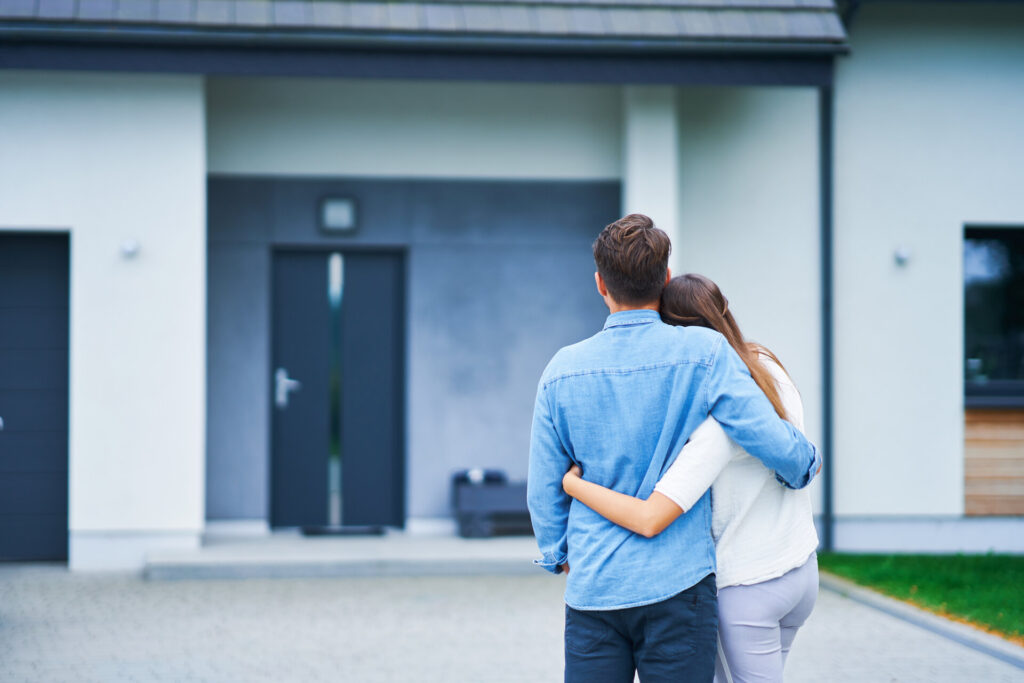 Ehepaar vor einem Einfamilienhaus in einer modernen Wohngegend