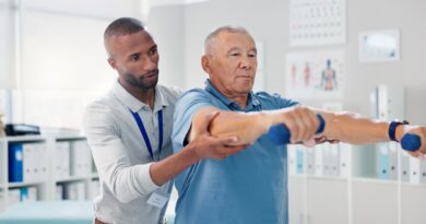 Ein Pflegehelfer unterstützt einen älteren Patienten bei physiotherapeutischen Übungen mit Hanteln in einer modernen Pflegeeinrichtung.