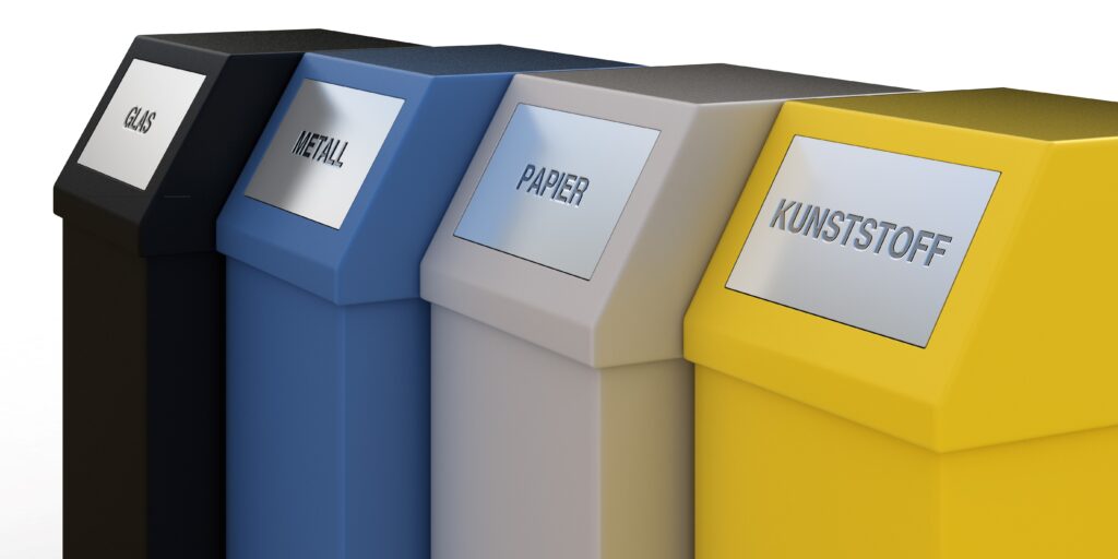 Vier farbcodierte Mülltrennungsbehälter in Schwarz (Glas), Blau (Metall), Grau (Papier) und Gelb (Kunststoff) zur effizienten Mülltrennung und Recycling.