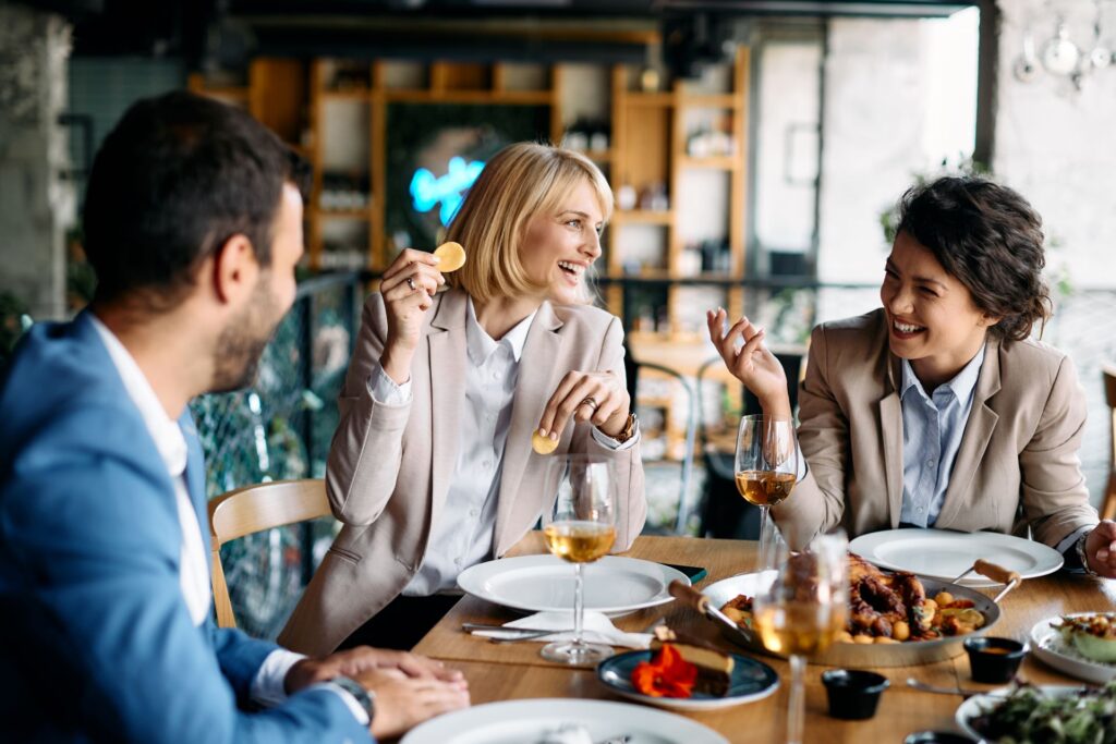 Eine Gruppe von Geschäftsleuten genießt eine entspannte Mittagspause in einem Restaurant in Hannover, während sie sich angeregt unterhalten und gemeinsam lachen.