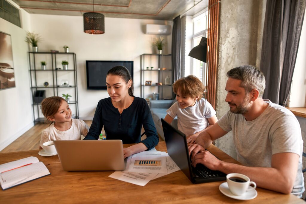 Eine Familie sitzt an einem Tisch und schauen auf ein Laptop