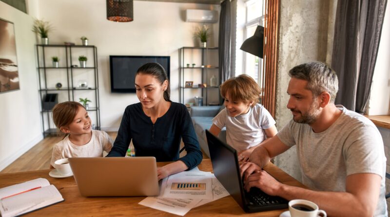 Eine Familie sitzt an einem Tisch und schauen auf ein Laptop