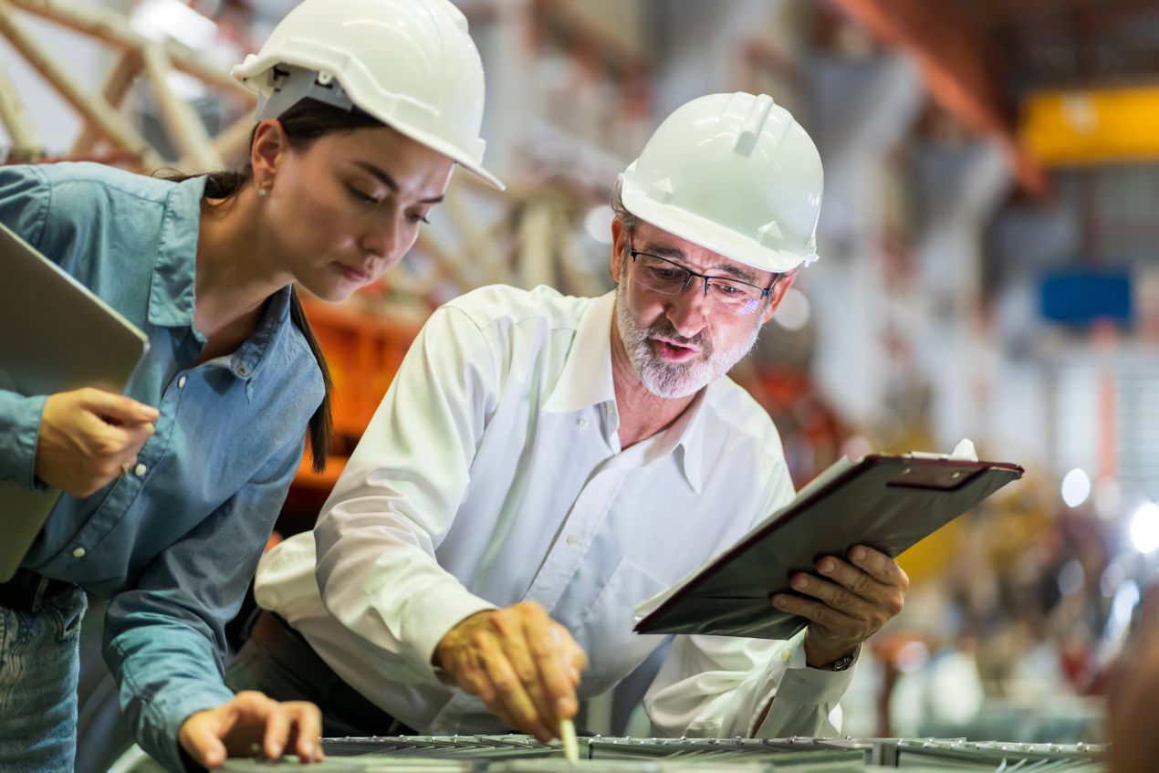 Technikerin und Ingenieur bei der Begutachtung einer gebrauchten Biegemaschine in der Produktionshalle