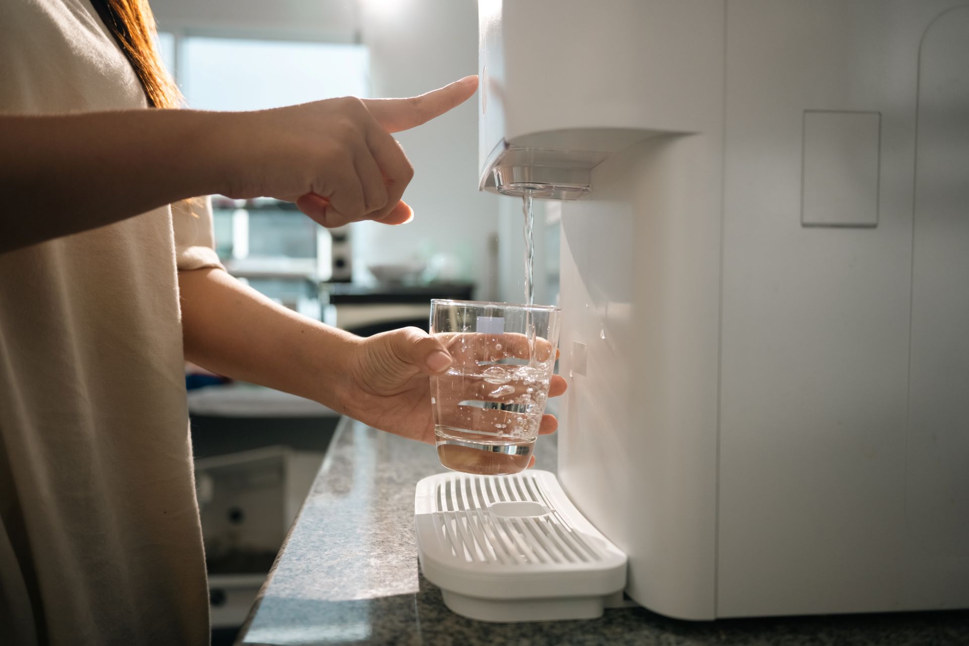 Eine Hand füllt ein Glas mit Wasser an einem kompakten Küchengerät – zeigt die Anwendung einer Wasserfilteranlage in der Küche im Alltag
