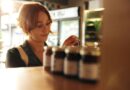 Junge Frau im Laden hält ein Glas mit Produktetikett in der Hand – Gestaltung und Information auf dem Etikett beeinflussen ihre Kaufentscheidung