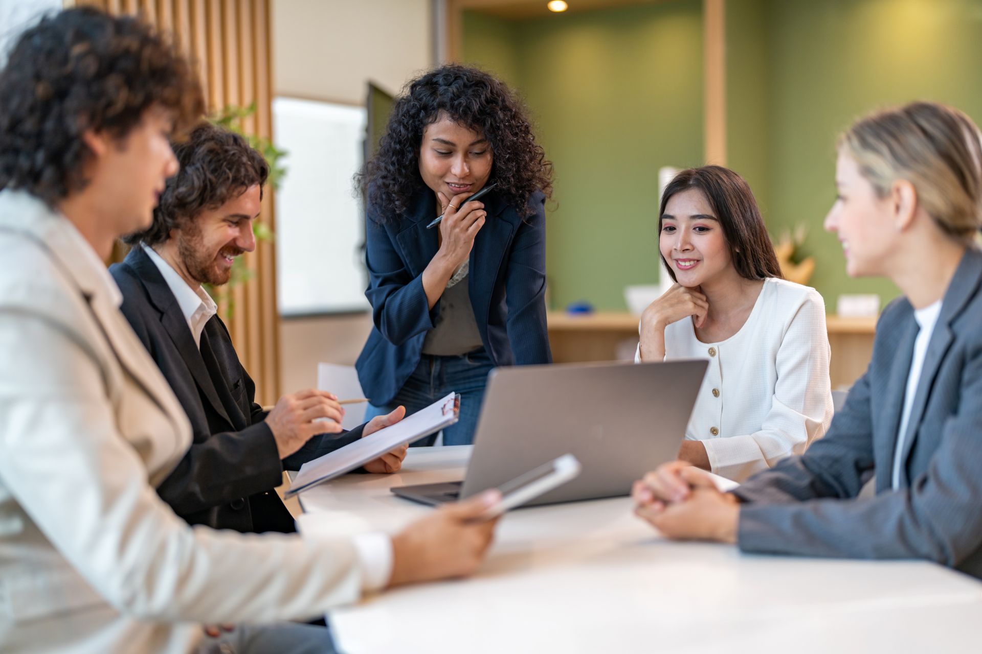 Vier Geschäftsleute und eine Beraterin diskutieren gemeinsam vor einem Laptop in einem modernen Büro während eines strategischen Meetings.