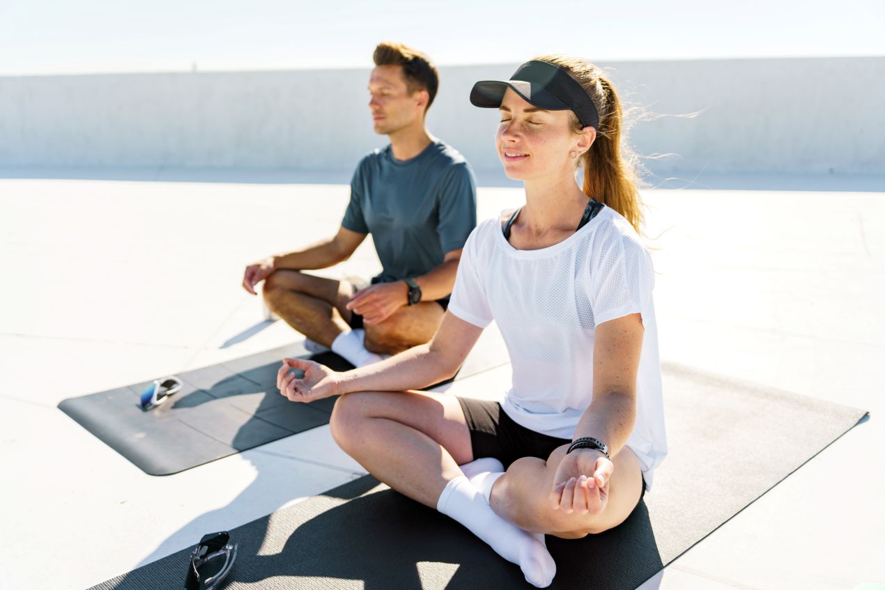 Zwei Erwachsene sitzen im Schneidersitz auf einer Dachterrasse und machen gemeinsam Breathwork bei sonnigem Wetter