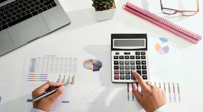 Person arbeitet mit Taschenrechner und Finanzunterlagen am Schreibtisch | Rechnungsblöcke